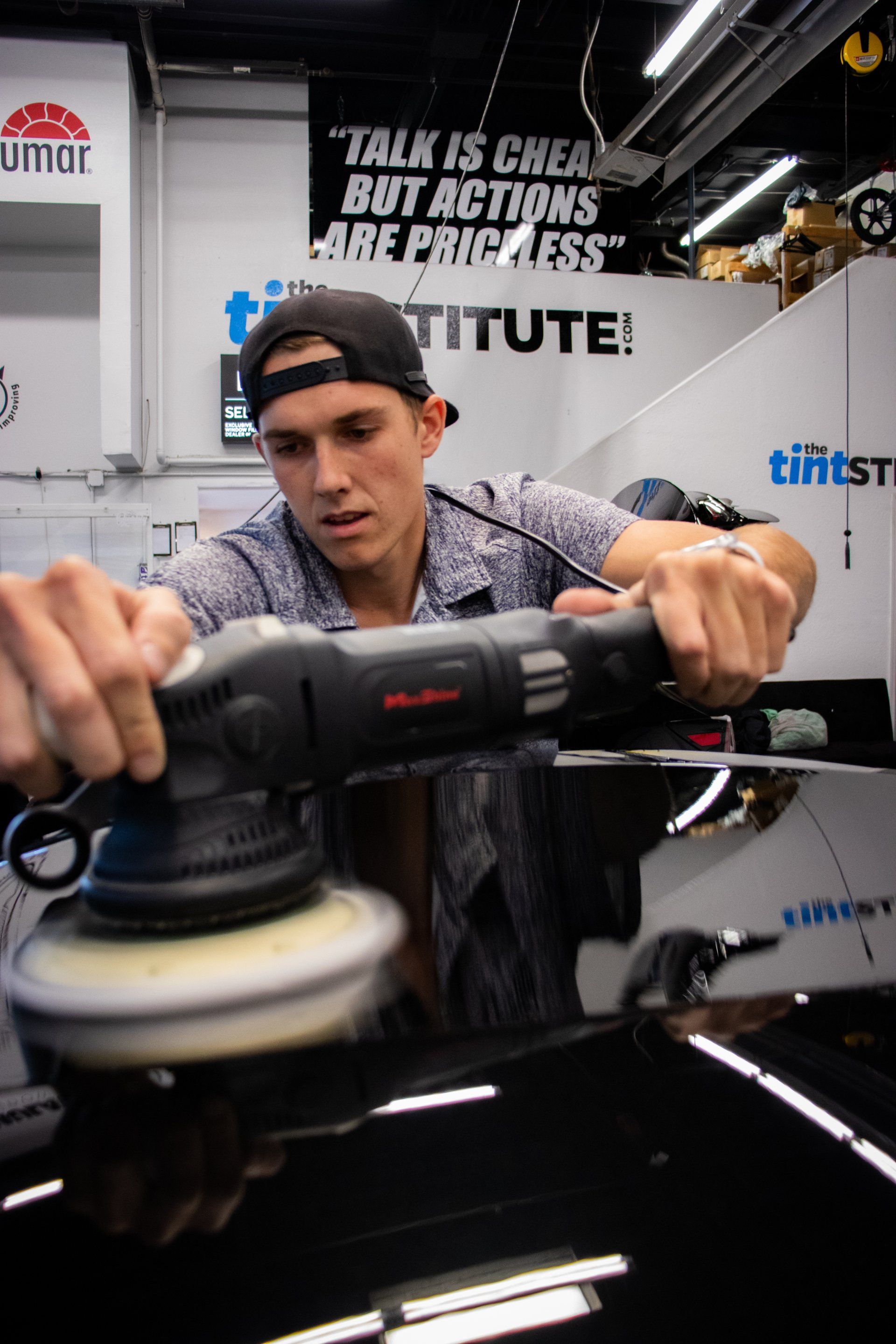 A man polishing a black car hood at an auto show booth with Tifin branding.
