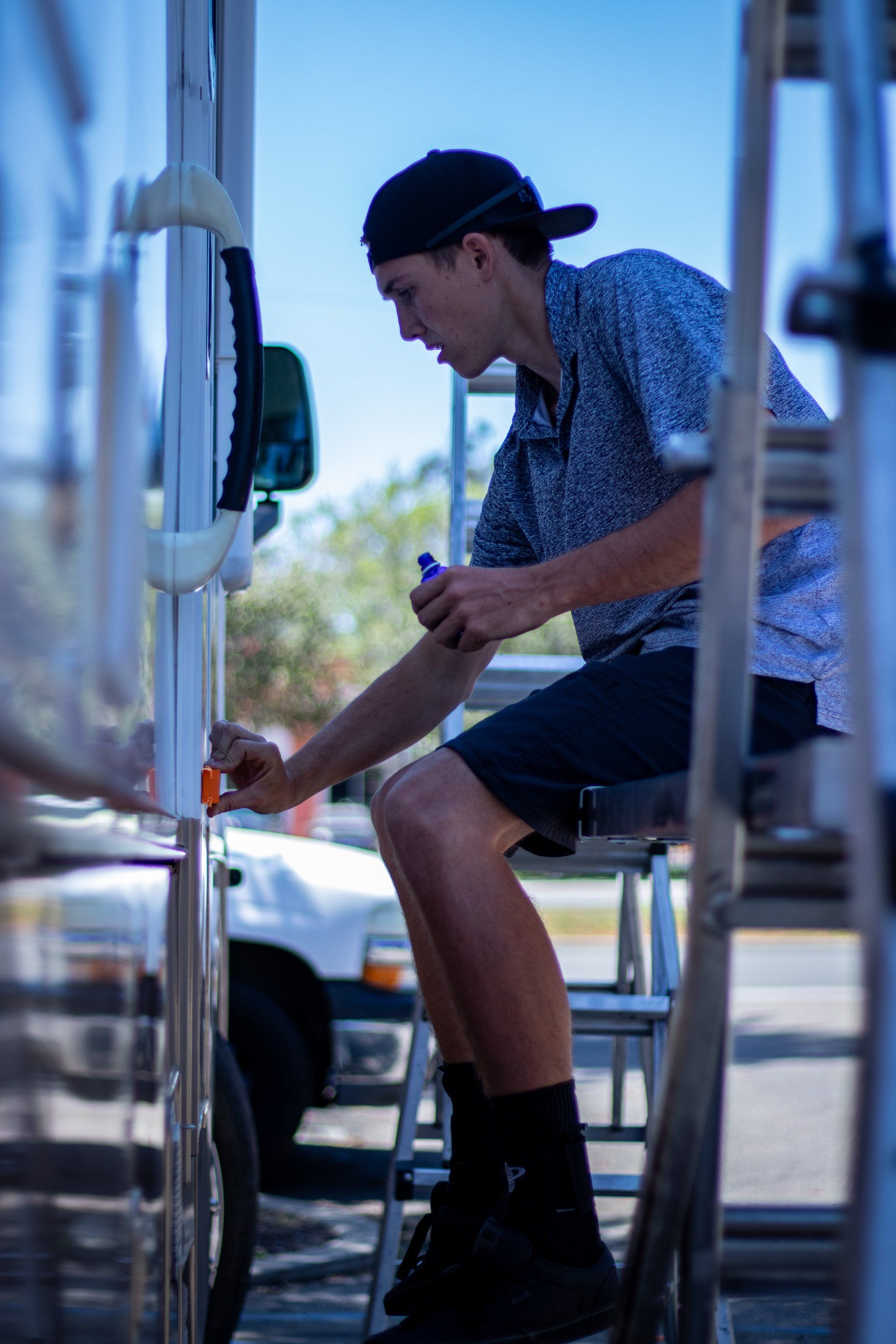 Person crouching beside a trailer, using a tool near the wheel on a sunny street