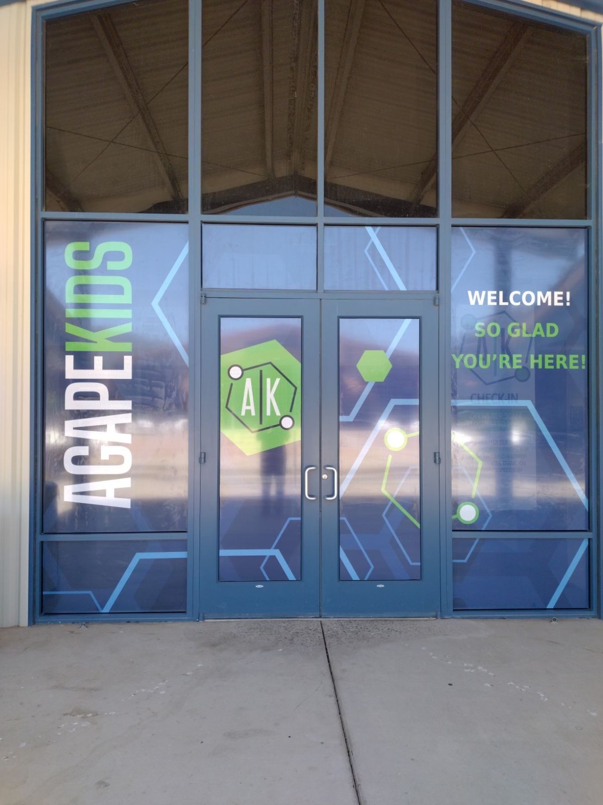 Storefront glass doors with blue “HAPPYKIDS” signage and a “WELCOME! SO GLAD YOU’RE HERE” message.