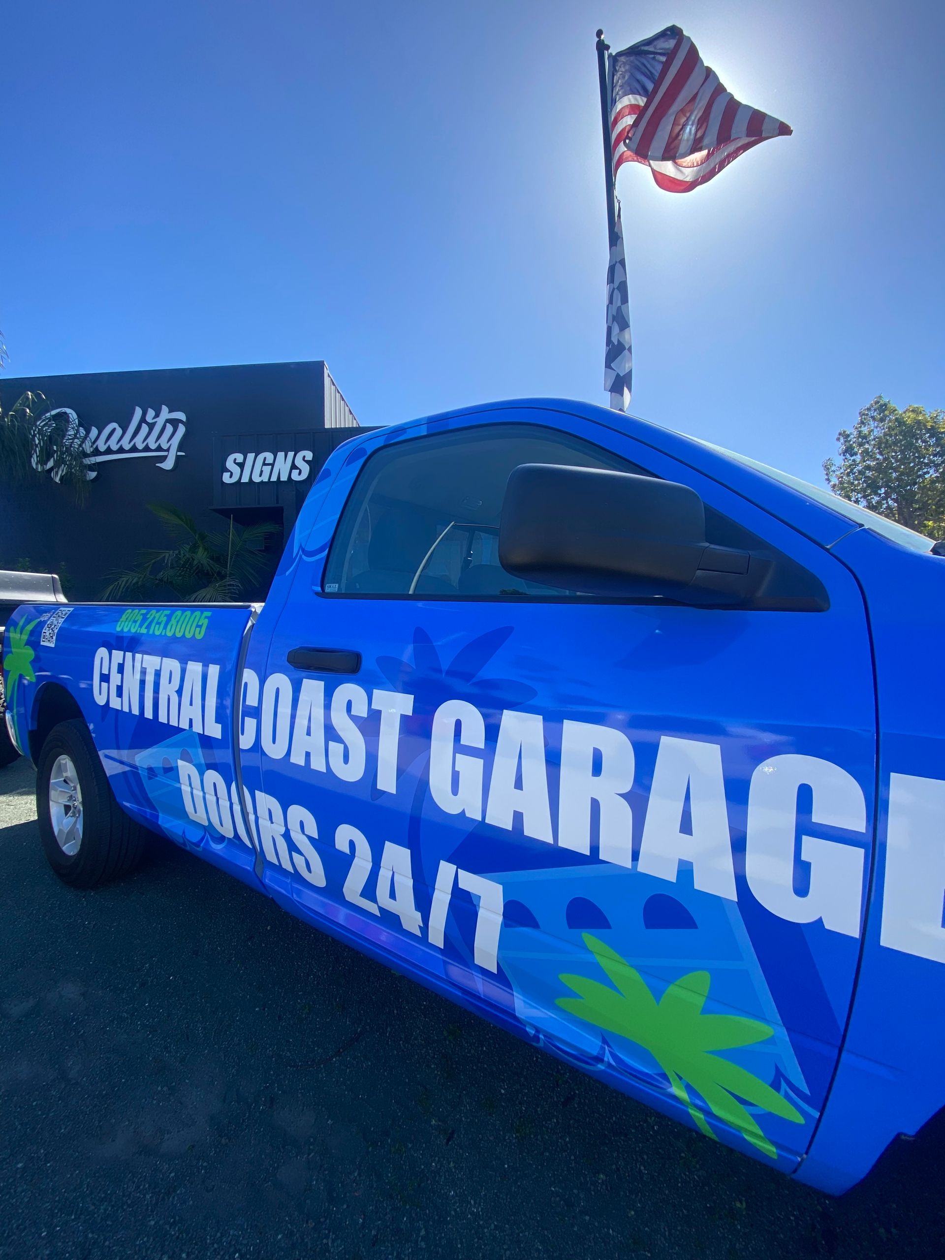 Blue Central Coast Garage work truck parked outside, with an American flag waving overhead.