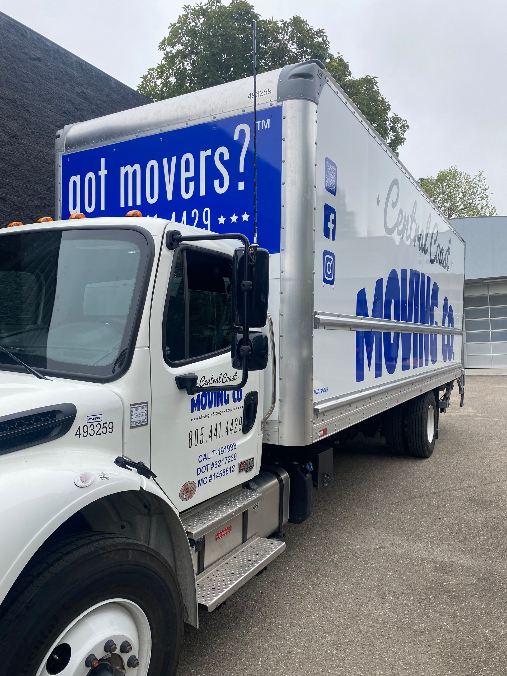 White box truck with blue “got movers?” branding parked on a road beside trees