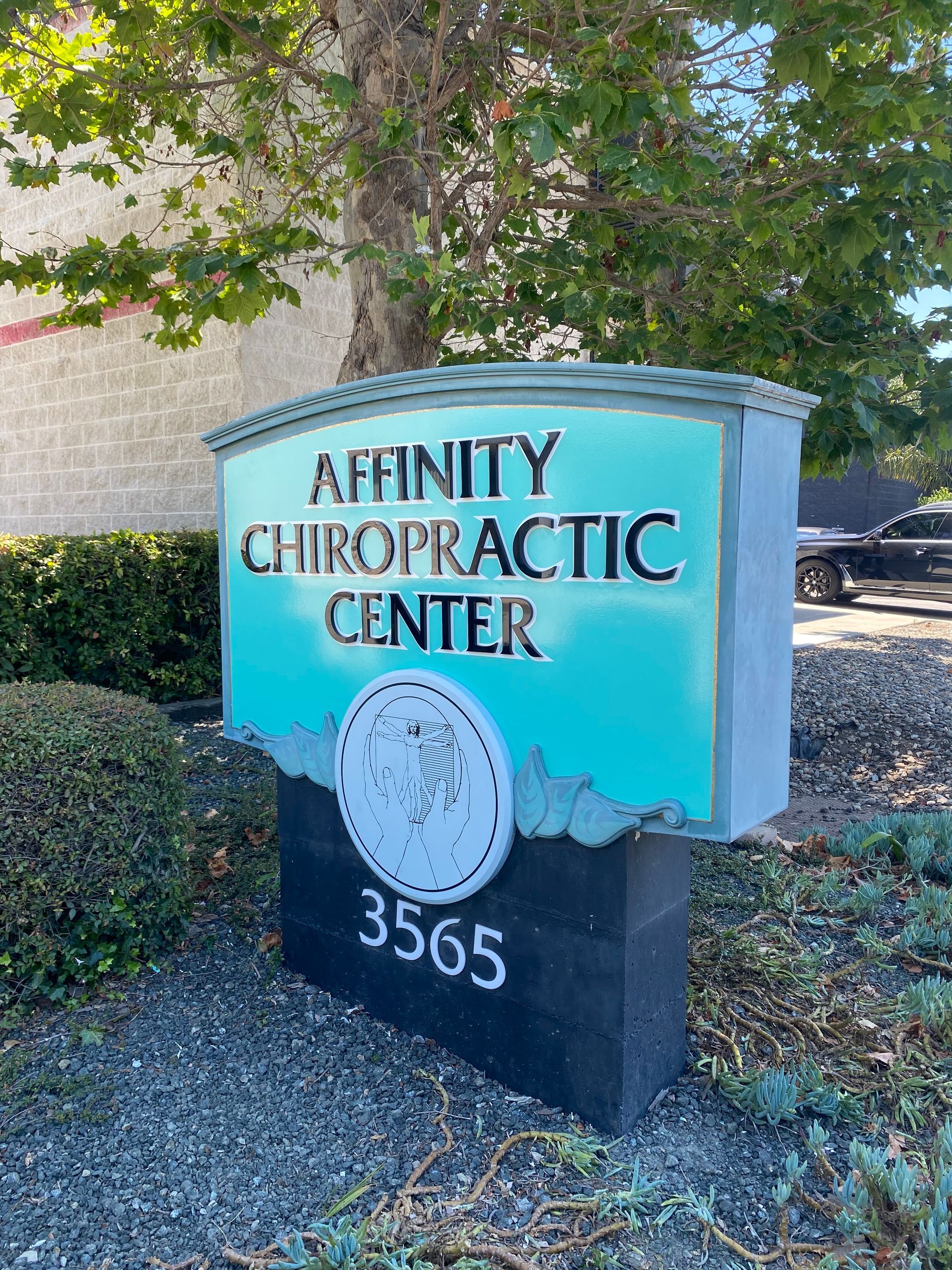 Sign for Infinity Chiropractic Center, turquoise and black, with address 3565 outside a building