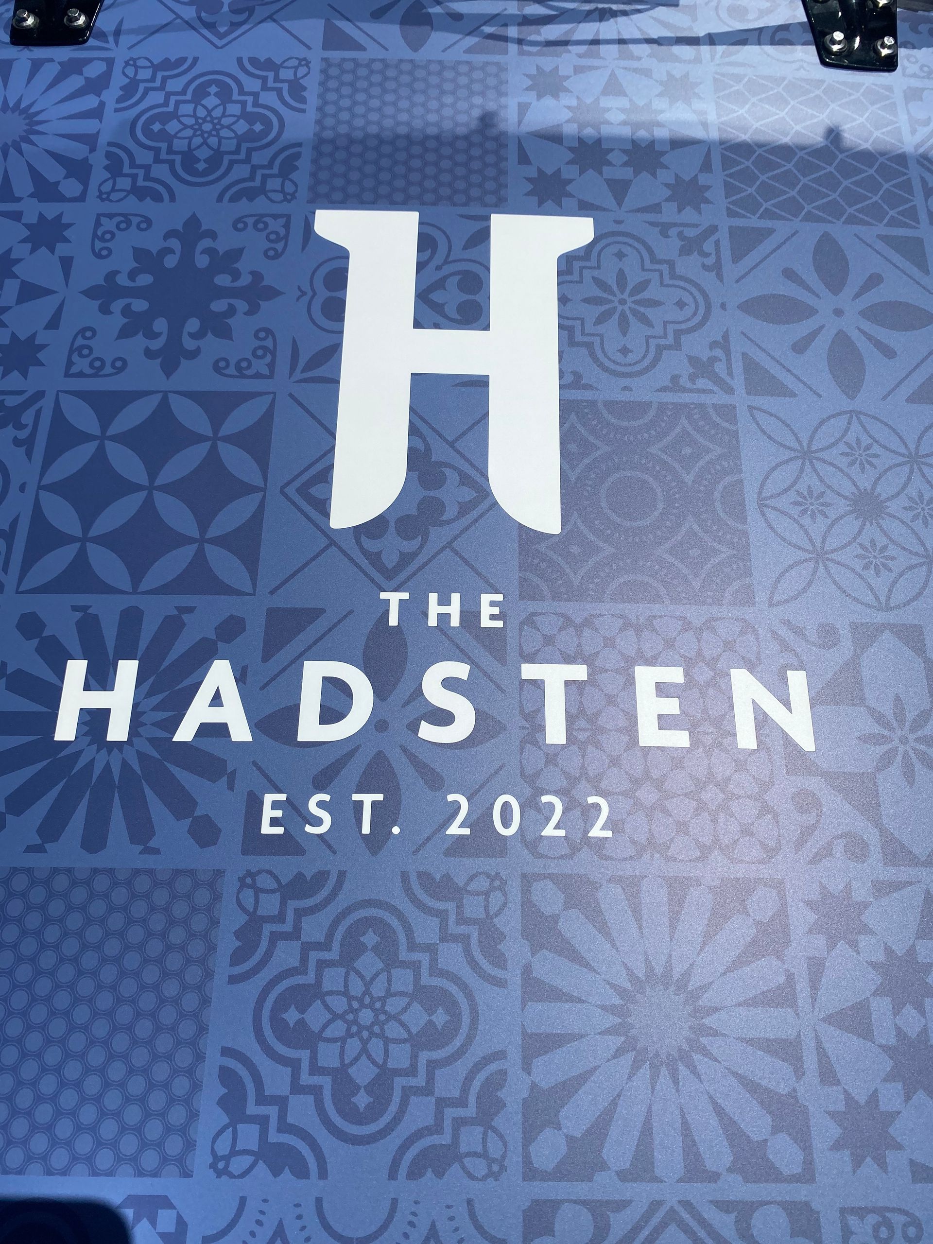 Blue patterned logo reading “THE HADSTEN” with a large H and “EST. 2022” underneath