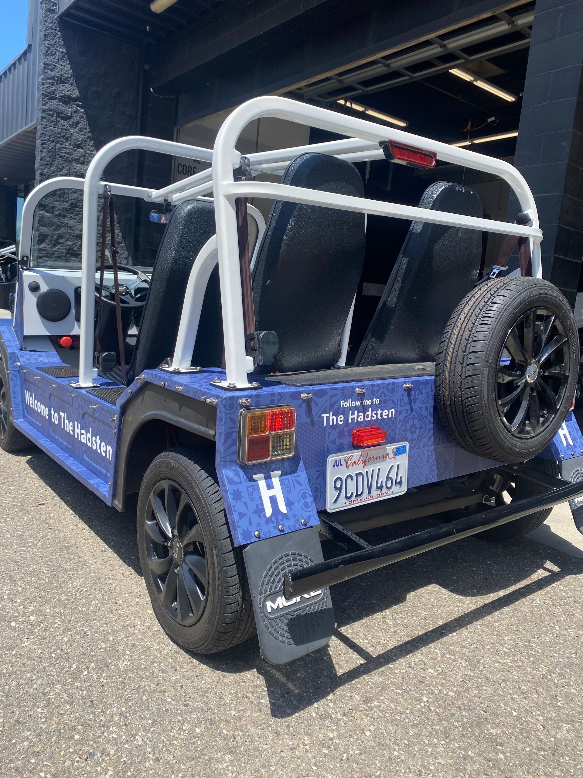 Blue off-road Jeep-style vehicle with roll cage and spare tire parked under a bridge