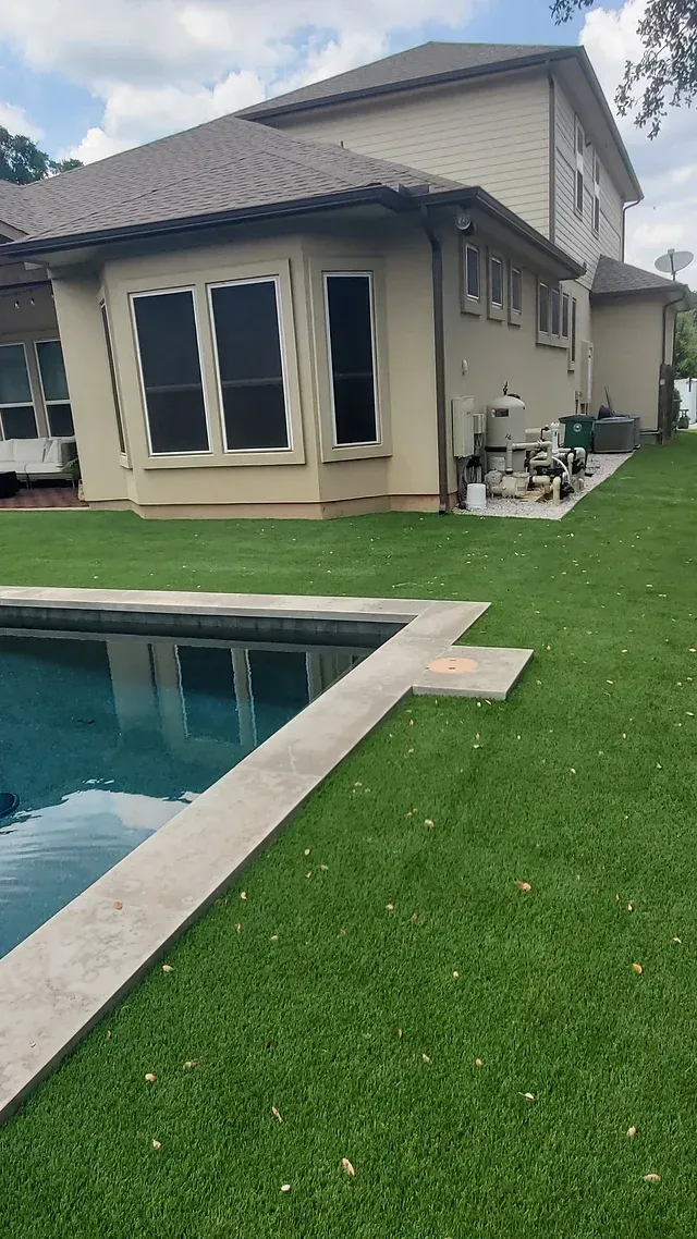 Backyard pool beside a beige house with a grassy lawn and stone pool deck