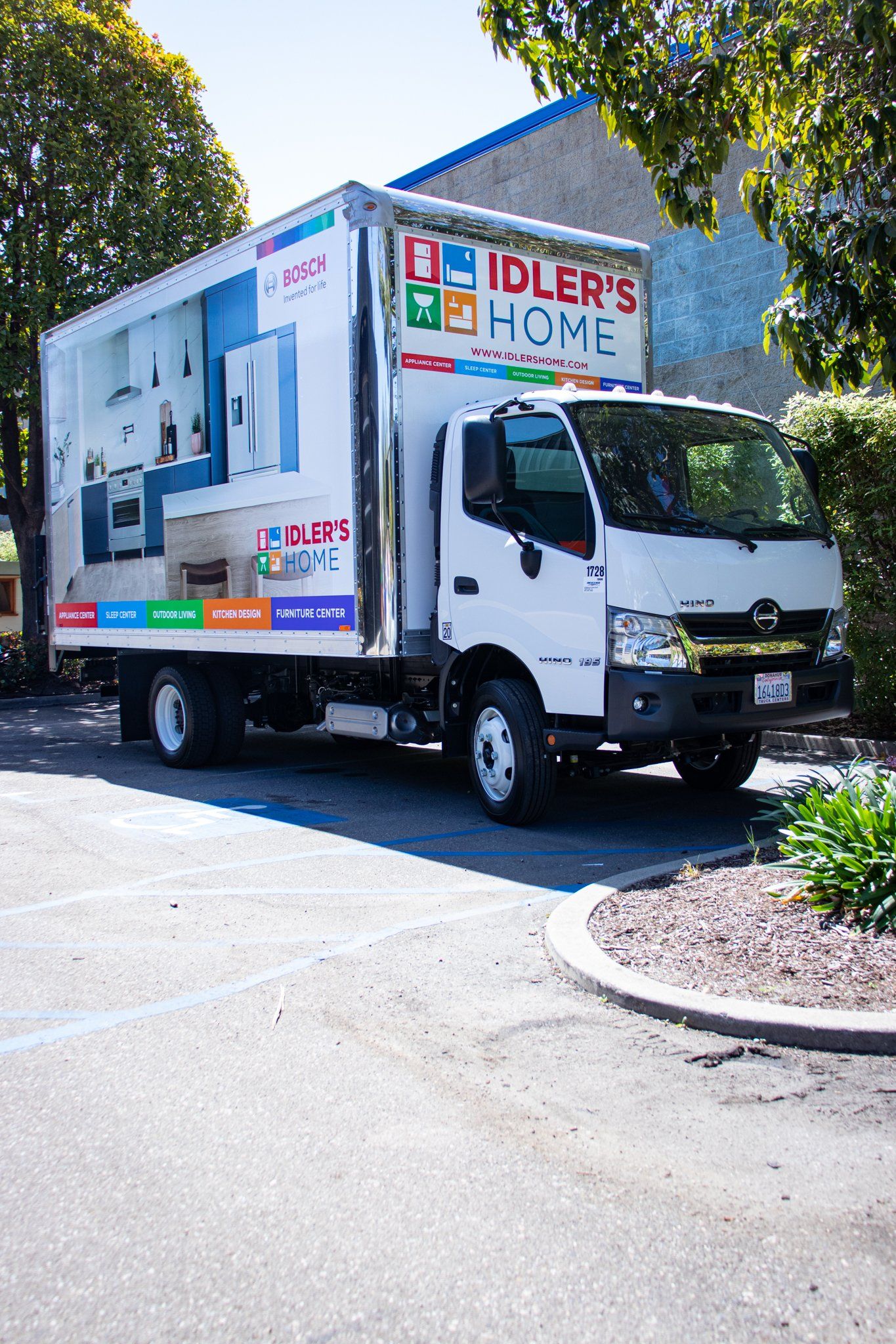 White delivery truck with colorful signs driving on a sunny road near trees and a curb