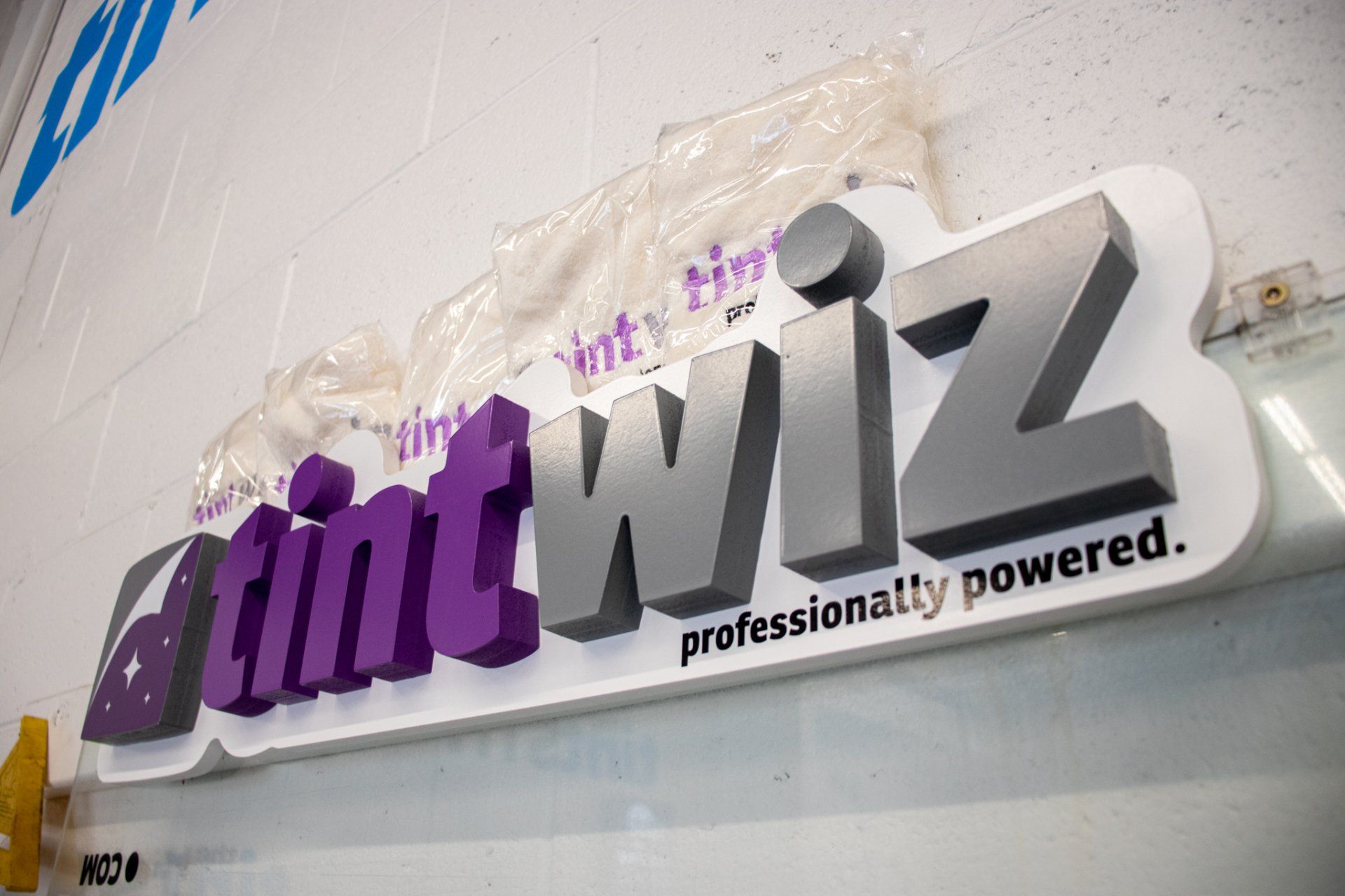 TintWiz logo sign in purple and gray on a white wall, with the tagline “professionally powered.”