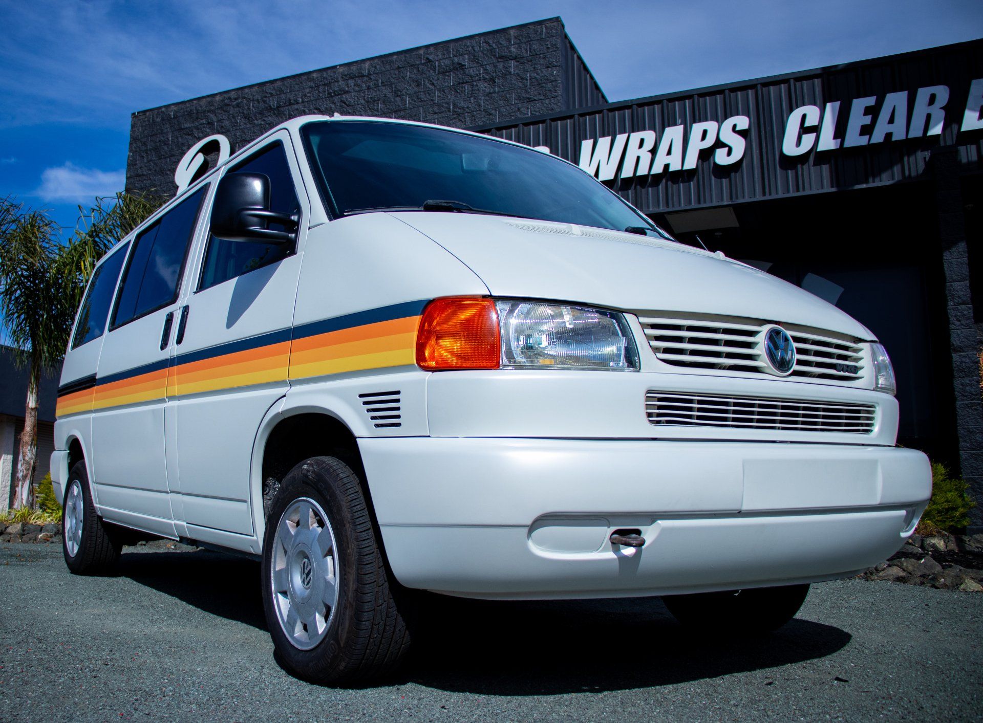 White van with orange and yellow stripe parked outside a shop with a “WRAPS” sign.