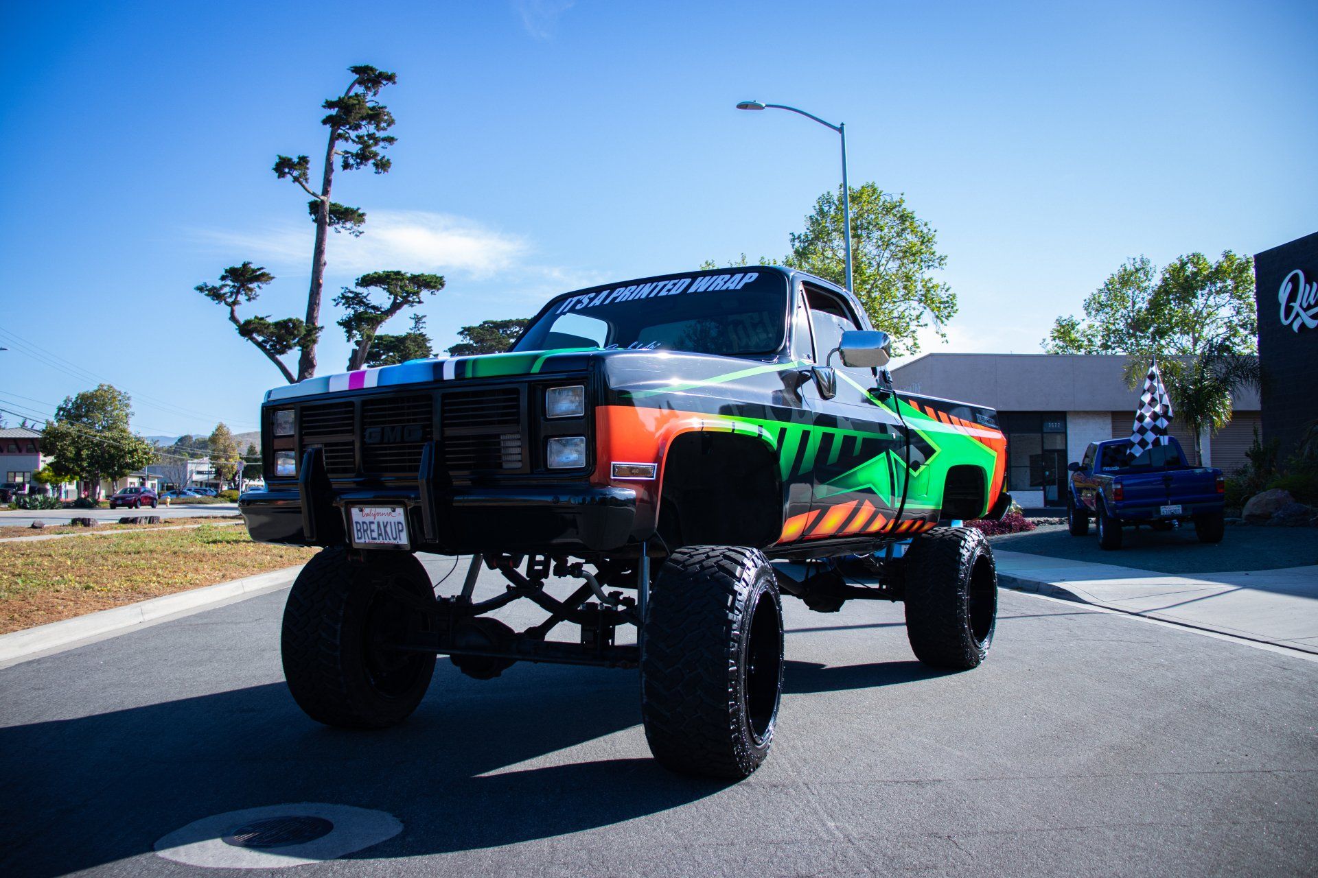 Lifted off-road truck with colorful wrap parked on a sunny street near houses.