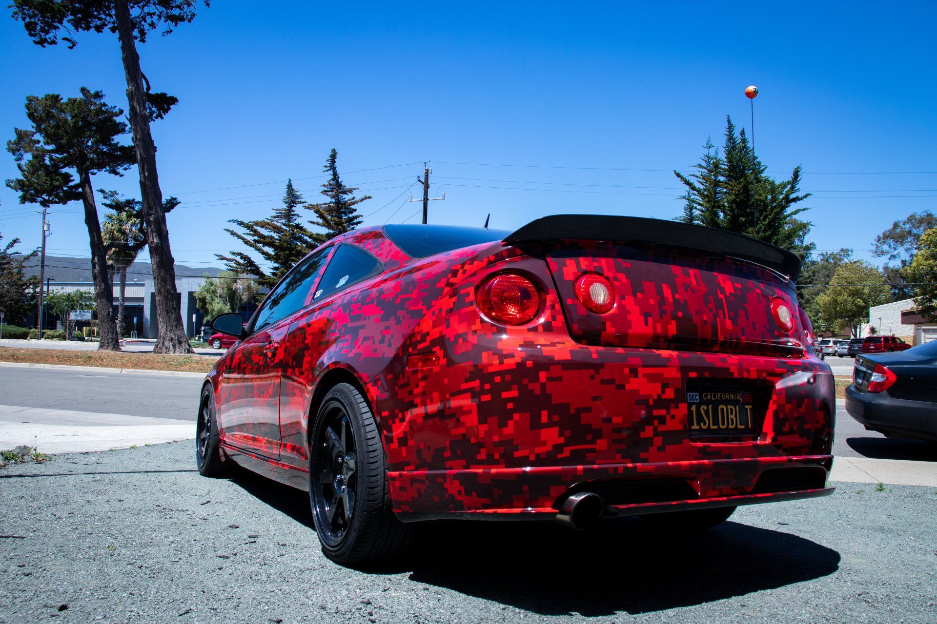 Red custom sports sedan parked outdoors on a sunny street, rear view with black wheels and tinted windows