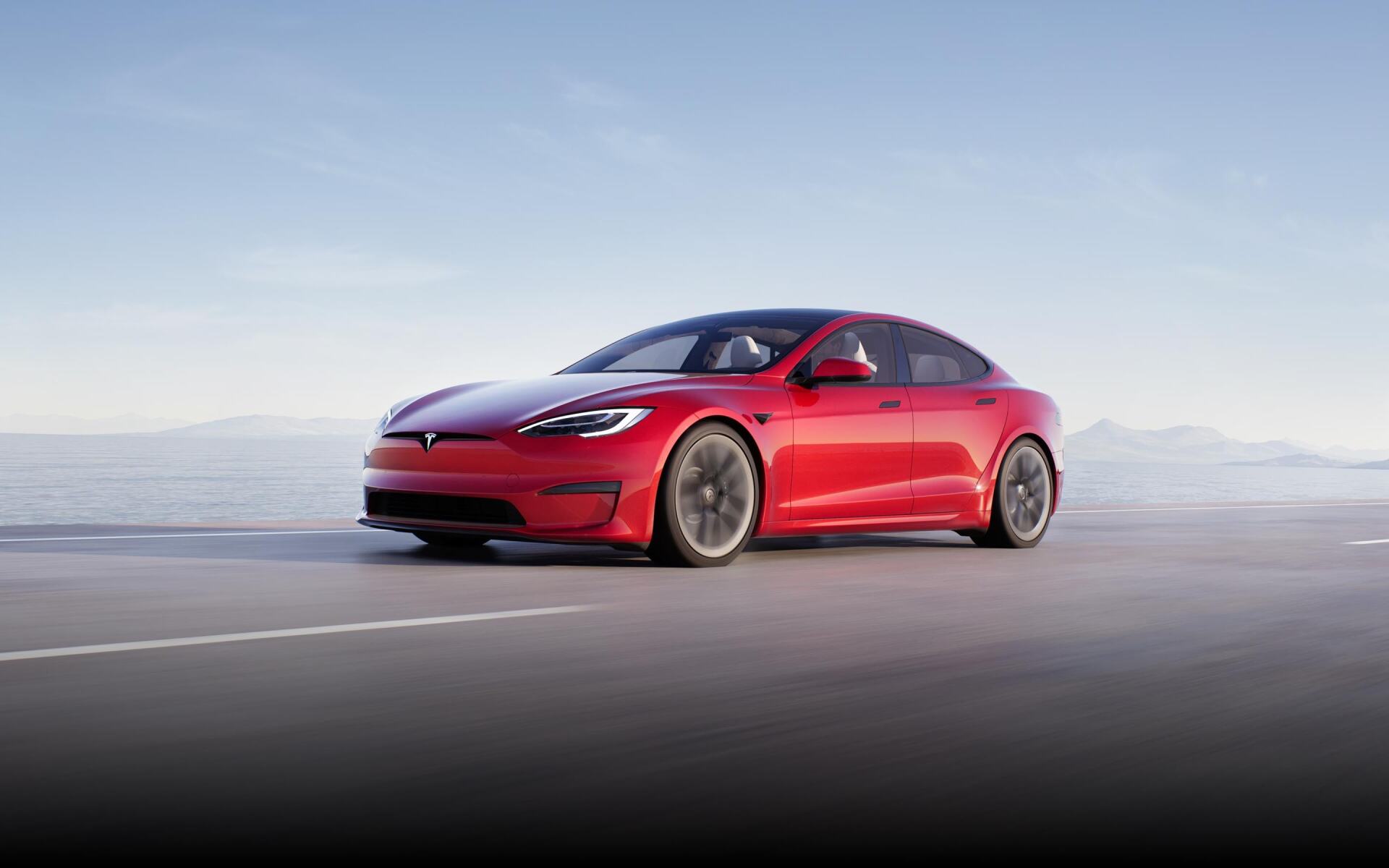 Red Tesla sedan driving on a flat road with mountains in the background