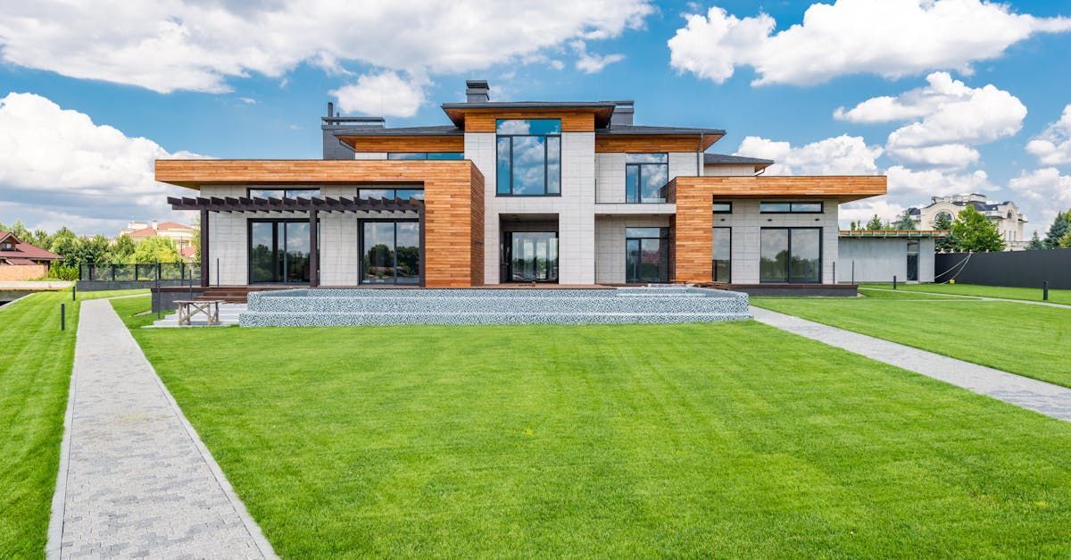 Modern two-story house with large windows, stone accents, and a wide green lawn under a bright sky