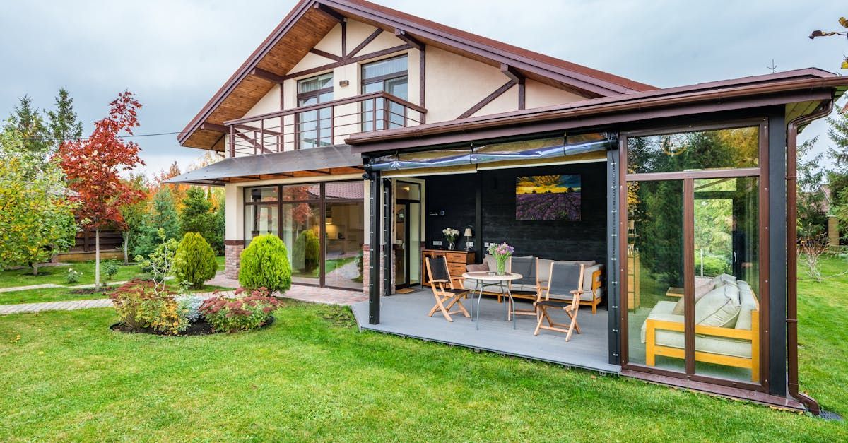 Modern house with a glass patio enclosure and outdoor seating on a green lawn