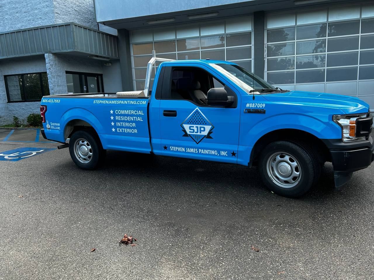 Blue pickup truck with company logo parked outside a building on a wet driveway