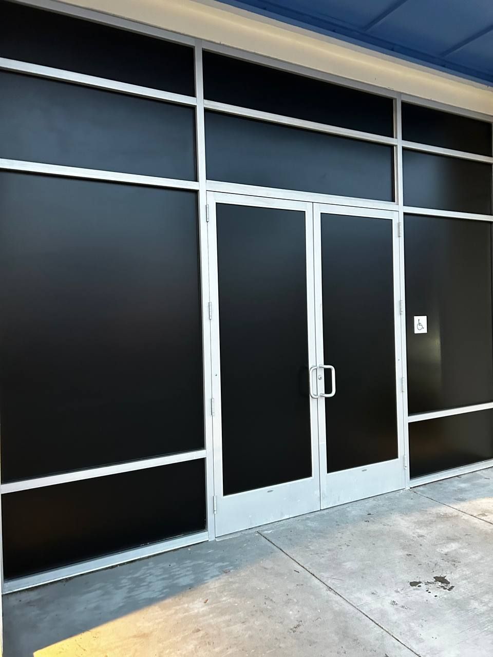 Glass double-door entrance with dark tinted windows and a concrete sidewalk outside