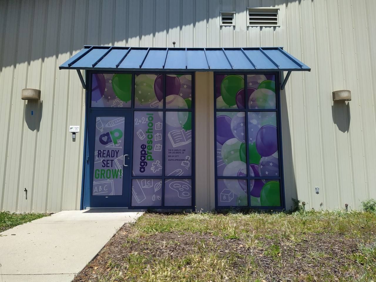 Storefront with colorful balloon-themed window art and a blue awning on a beige building