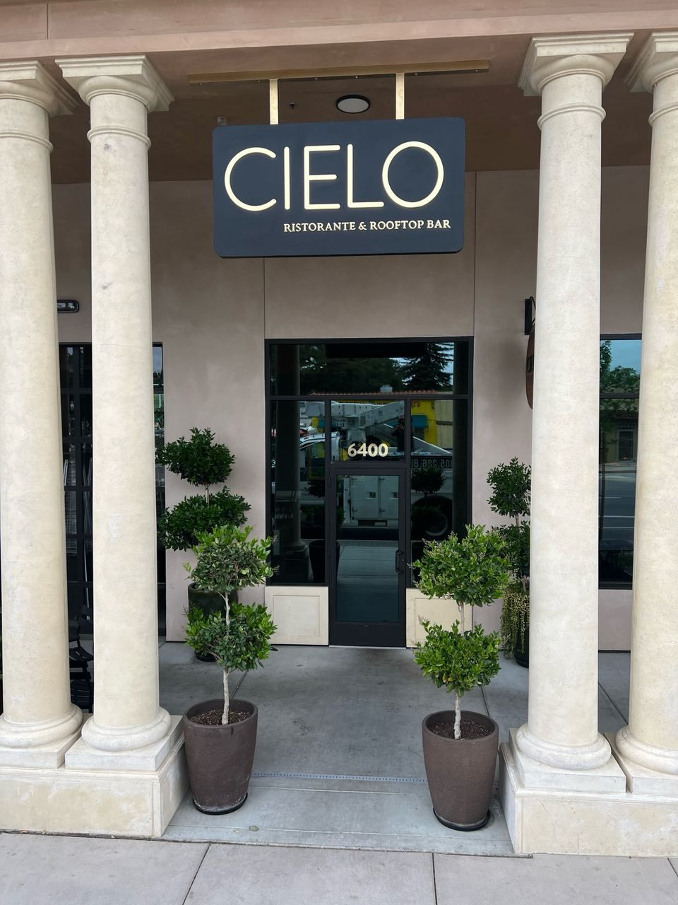 CIELO restaurant entrance with columns, potted plants, and glass door at a stone facade