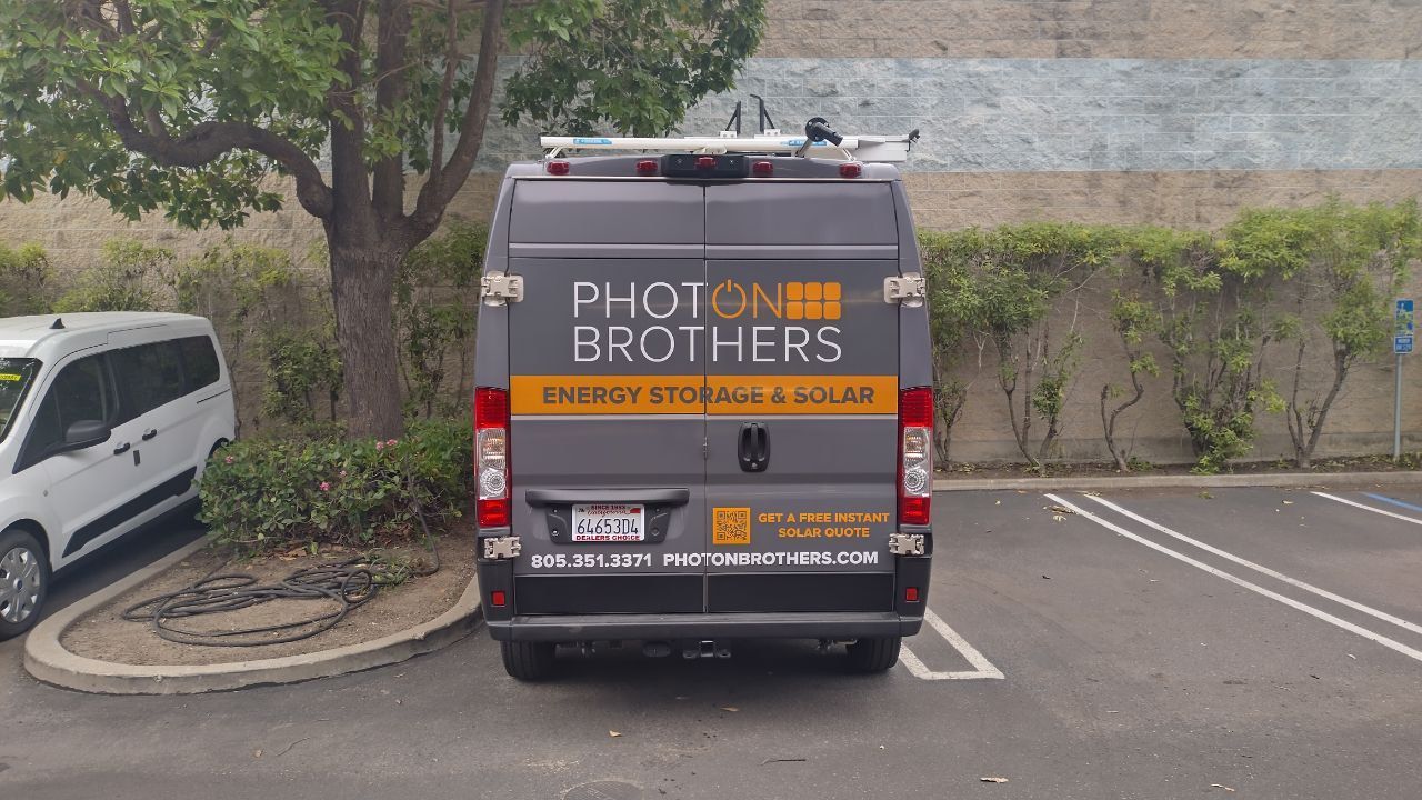Van parked in a lot with PHOTON BROTHERS signage and a small white vehicle nearby.