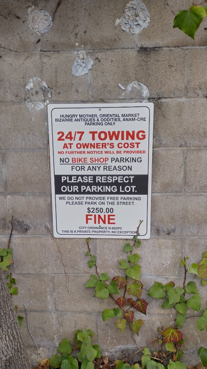 Tow-away warning sign on concrete wall, with red and black text and ivy growing nearby