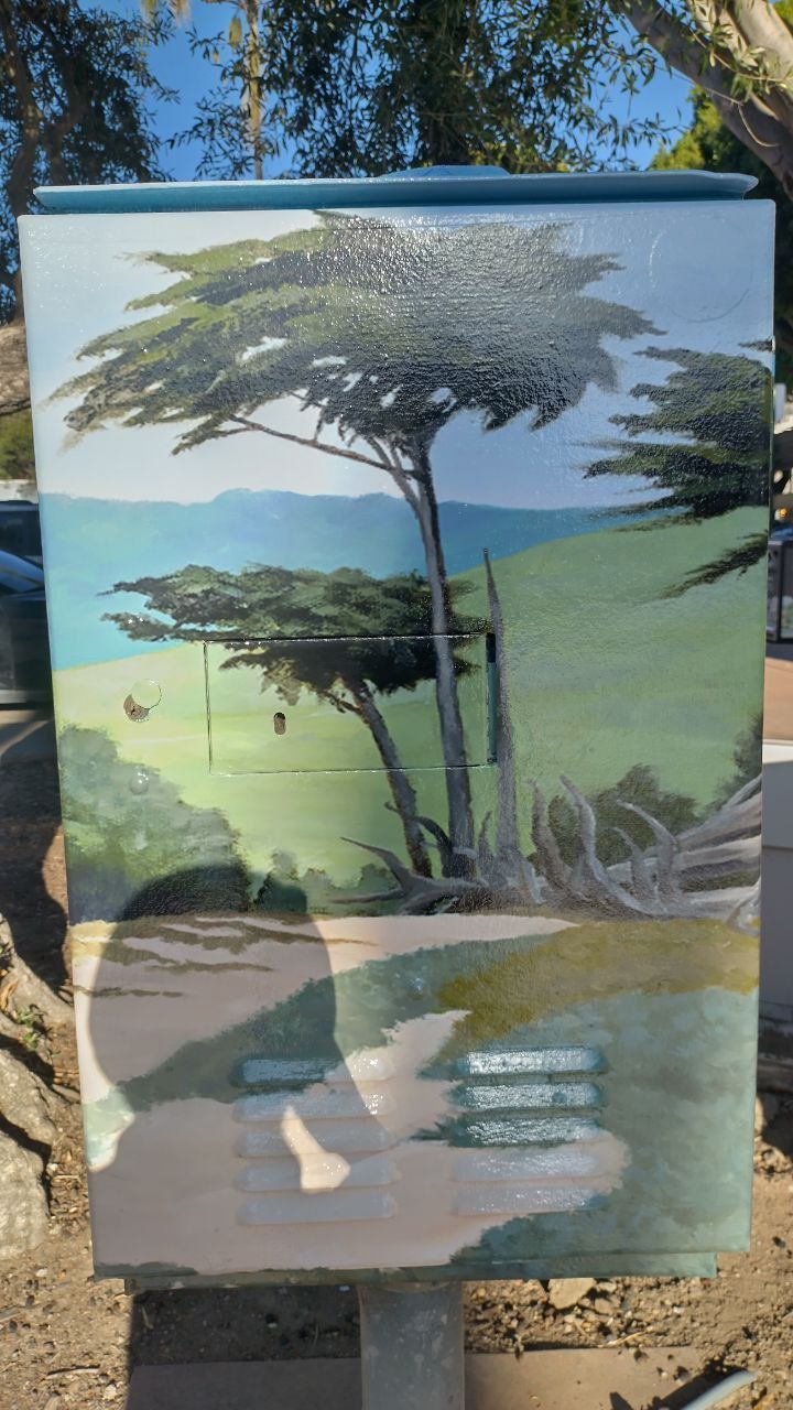 Tall tree in a green landscape painted on a rectangular sign outdoors.
