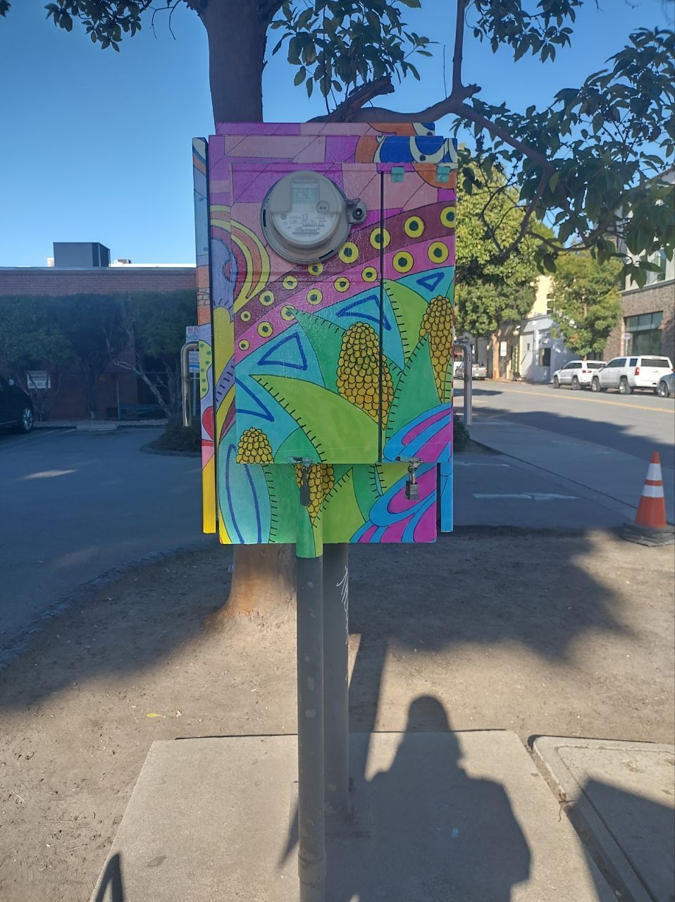 Colorful painted utility box on a sidewalk with abstract floral patterns and a round meter on the front.