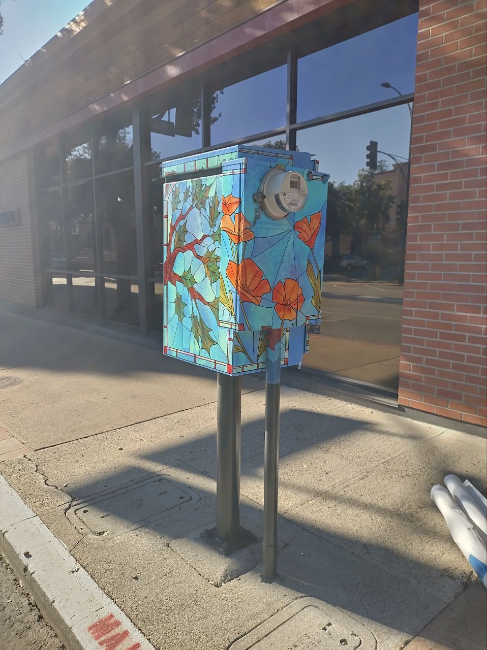 Painted utility box with colorful cartoon art on a sidewalk beside a brick storefront
