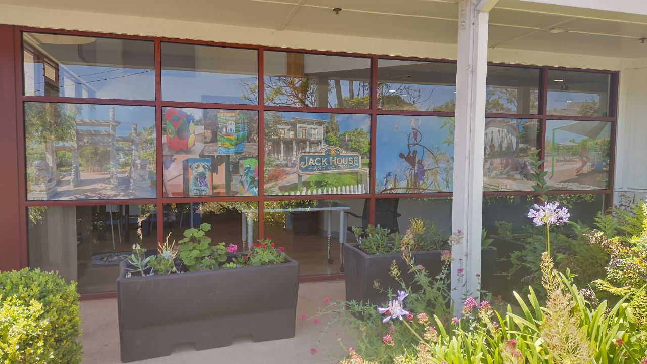 Storefront with large red-framed windows, potted flowers, and a covered walkway in front