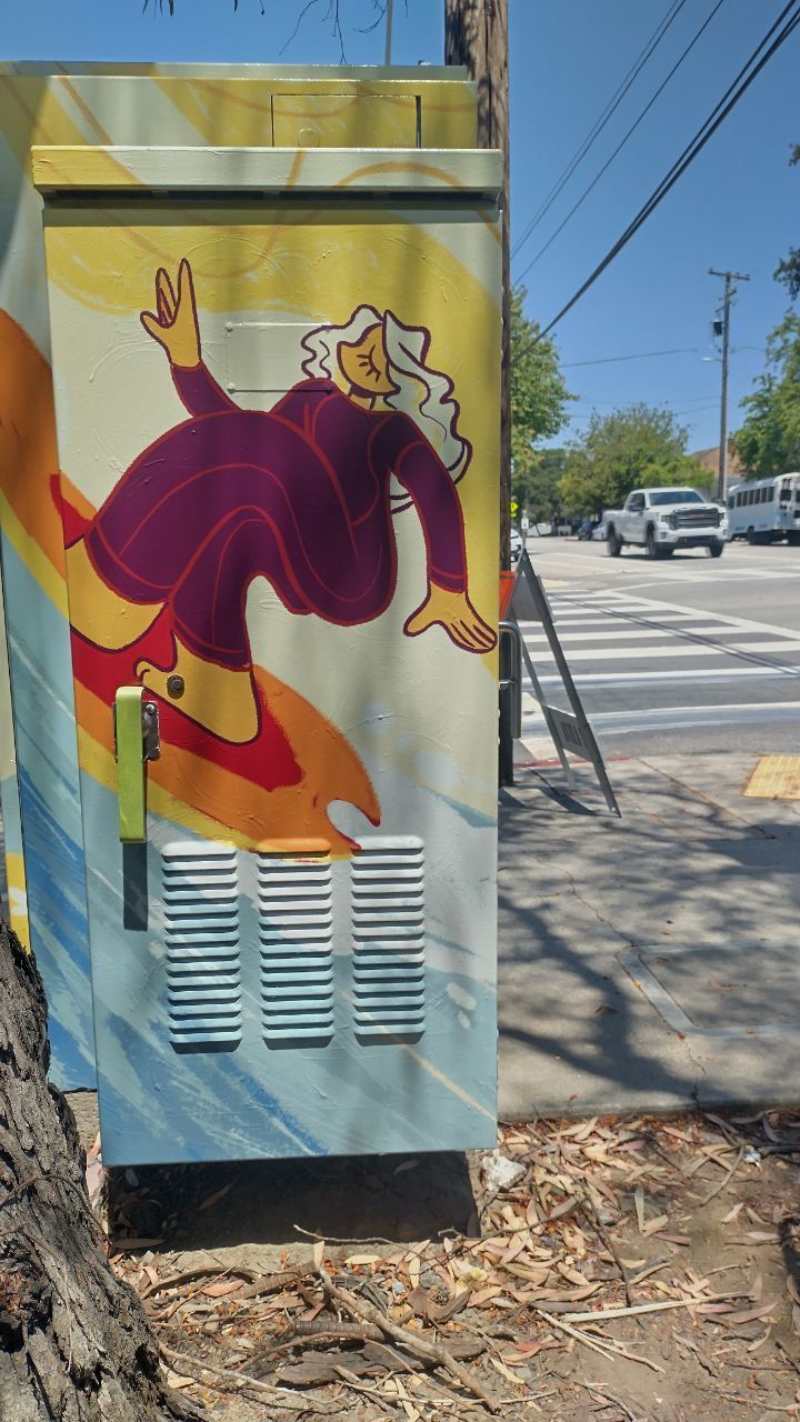 Colorful mural on a utility box beside a sidewalk, showing a purple-robed figure against a blue background.