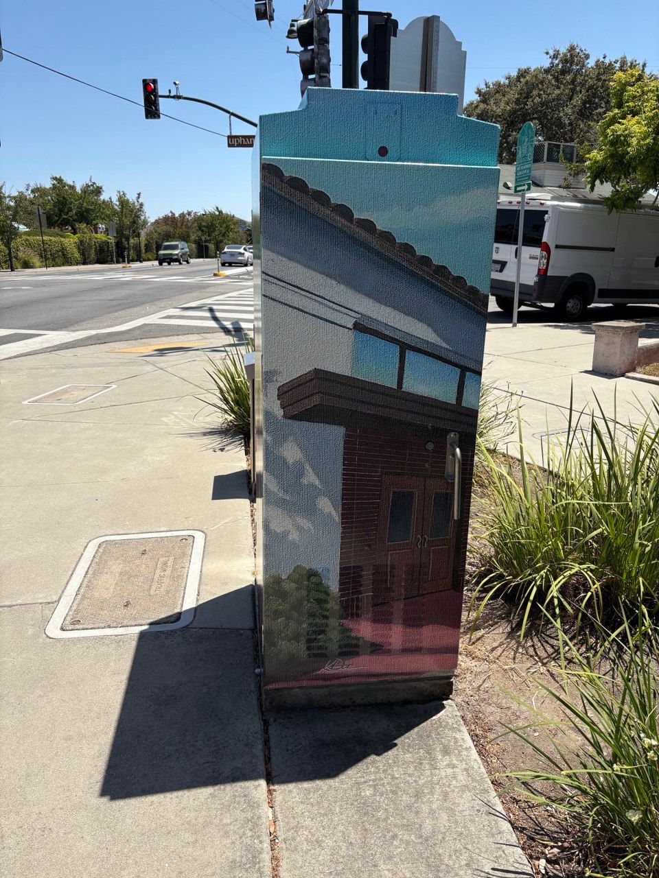 Mirror-finished utility box on a sunny sidewalk, reflecting nearby buildings and trees at an intersection
