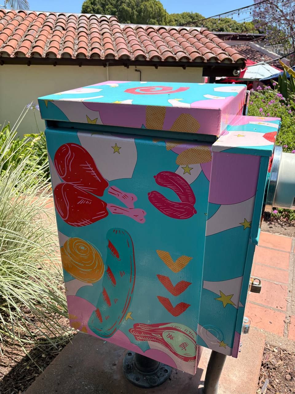 Colorful painted utility box with abstract flowers and leaves in a sunny garden patio setting