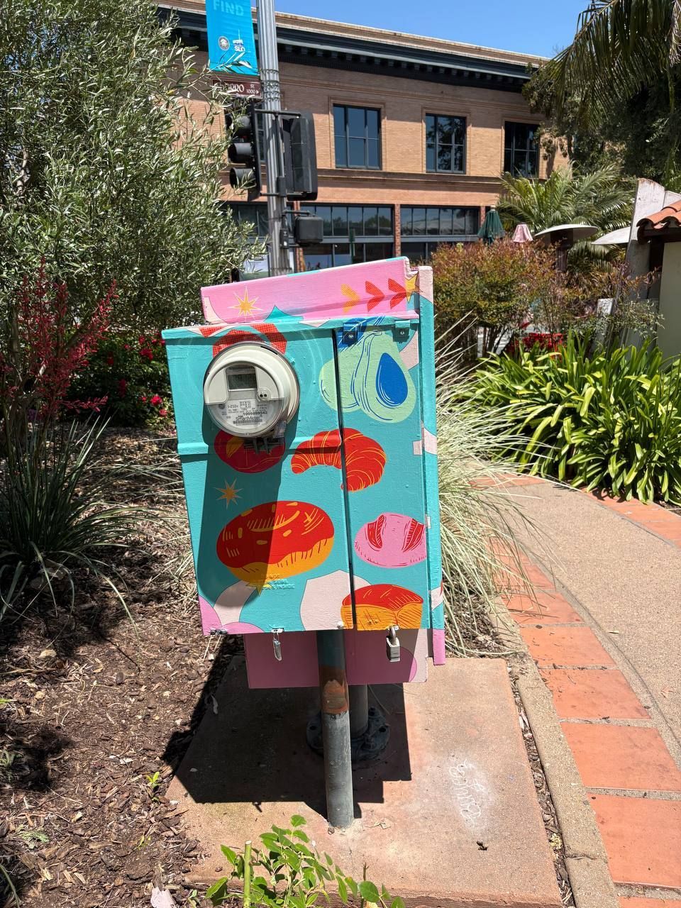 Colorful utility box with painted hearts and arrows beside a brick walkway in a garden courtyard