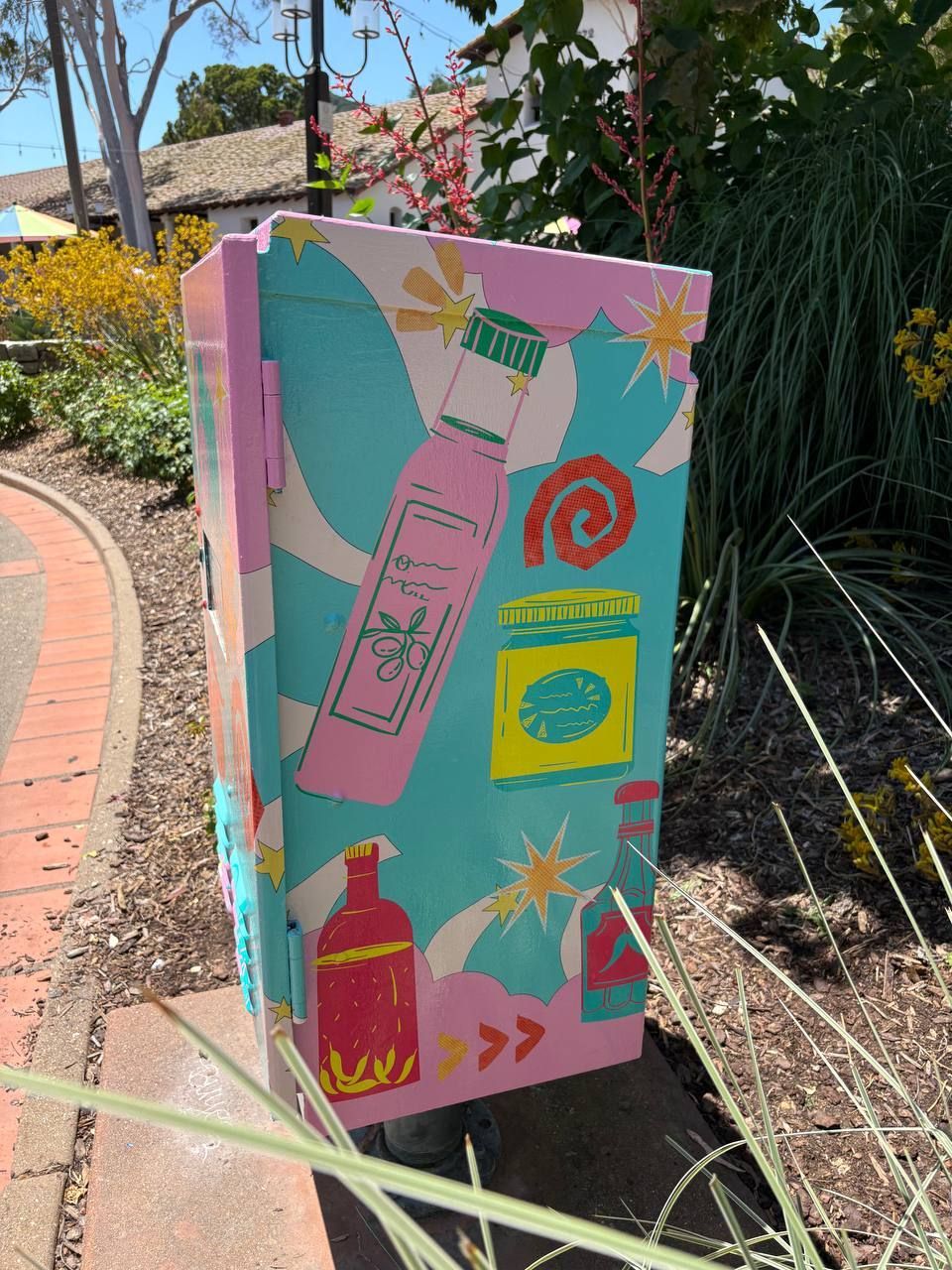 Colorful painted utility box with retro-style skincare and beauty illustrations beside a brick path