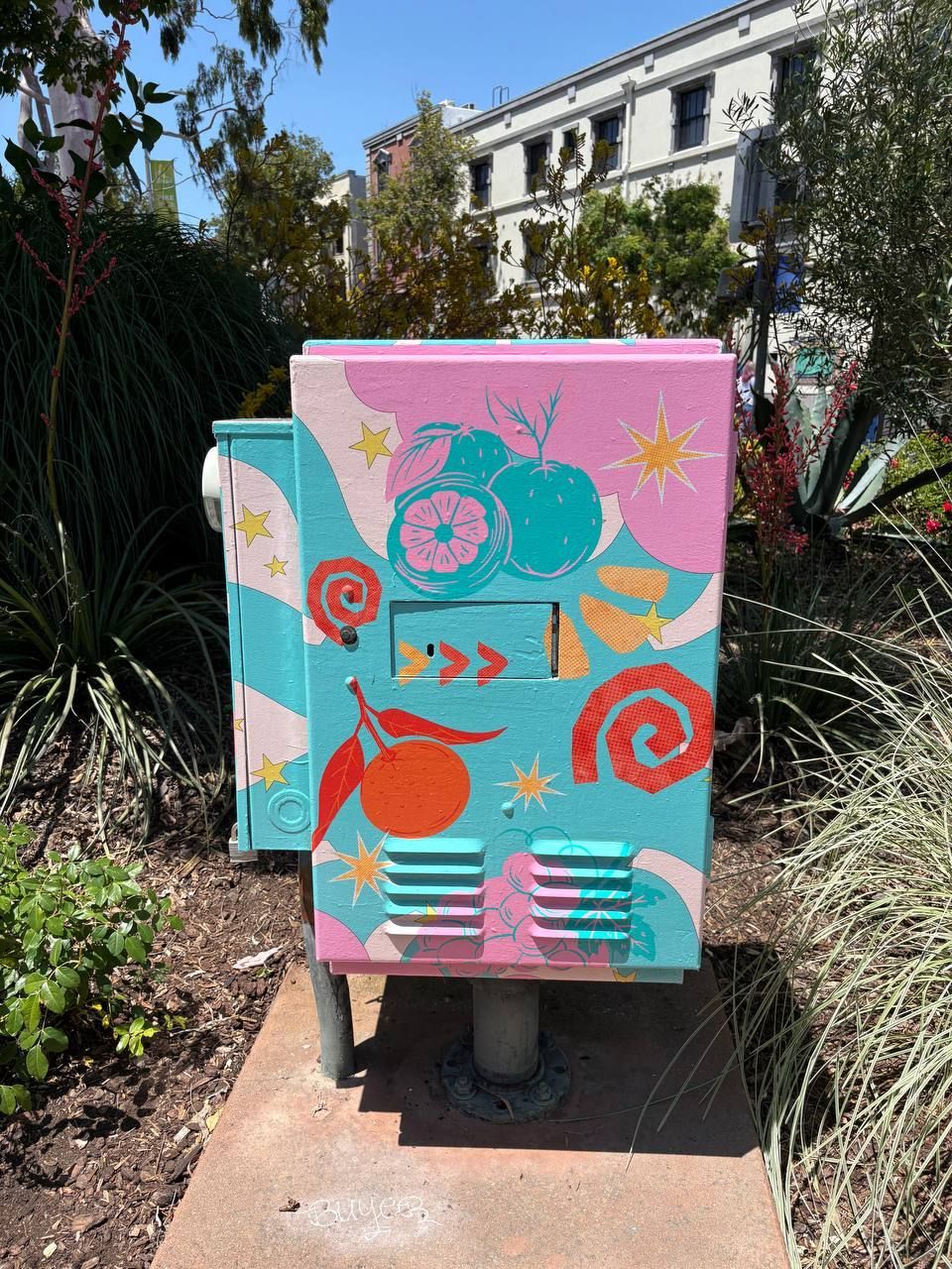 Colorful painted utility box with fish and sea-themed designs along a garden path outdoors