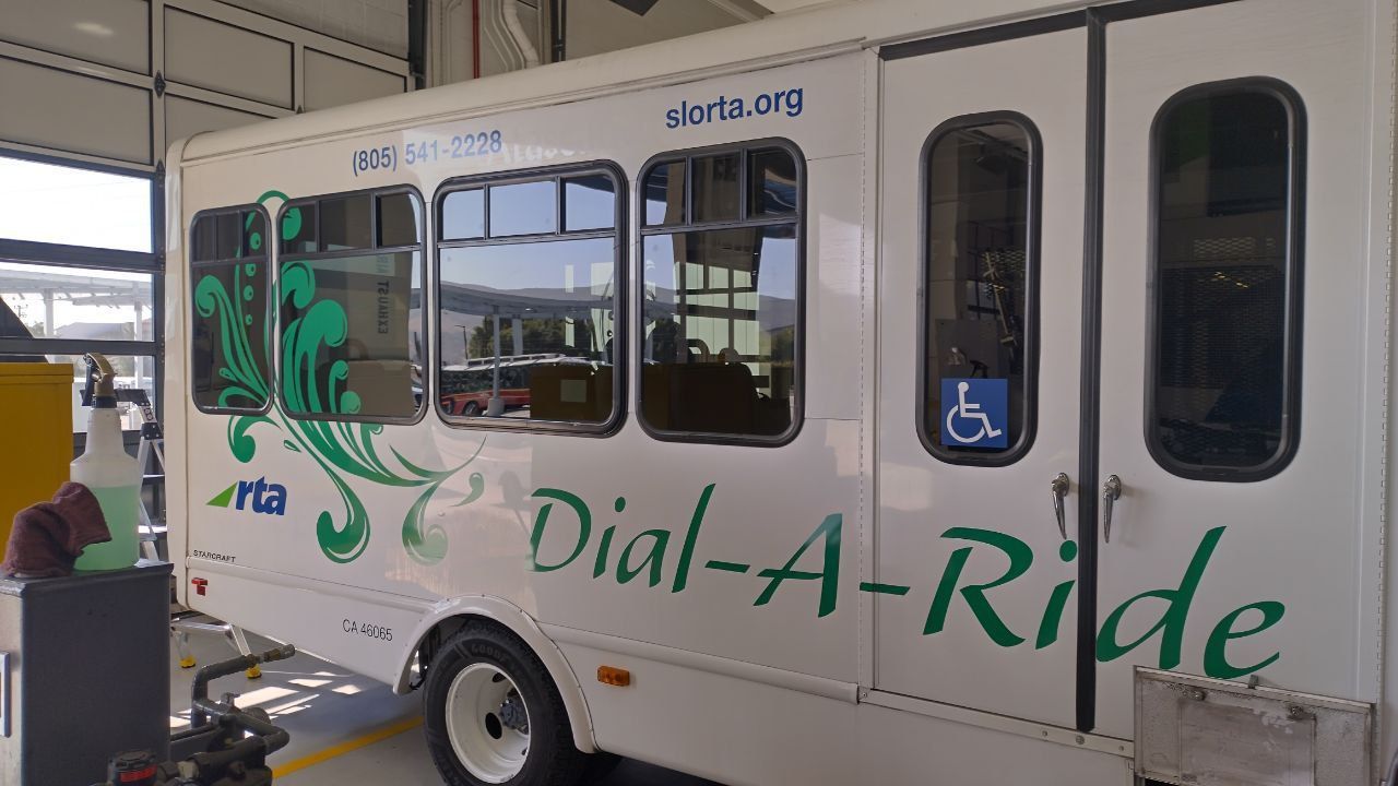White Dial-A-Ride shuttle bus with wheelchair accessibility symbol parked at a curb.