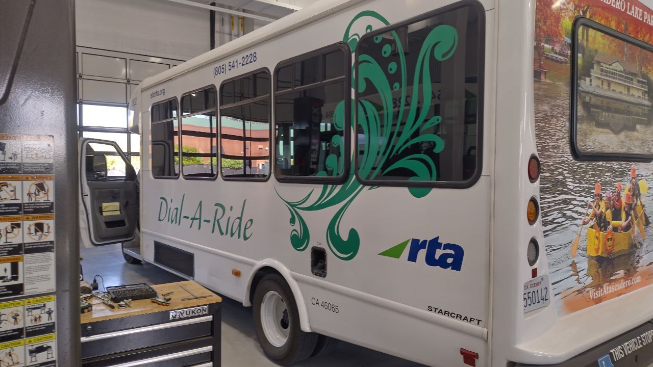 White paratransit shuttle with green floral graphics inside a garage bay, side view.