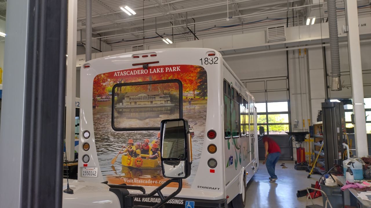 Back of a colorful bus in a garage, with a door open and workers nearby