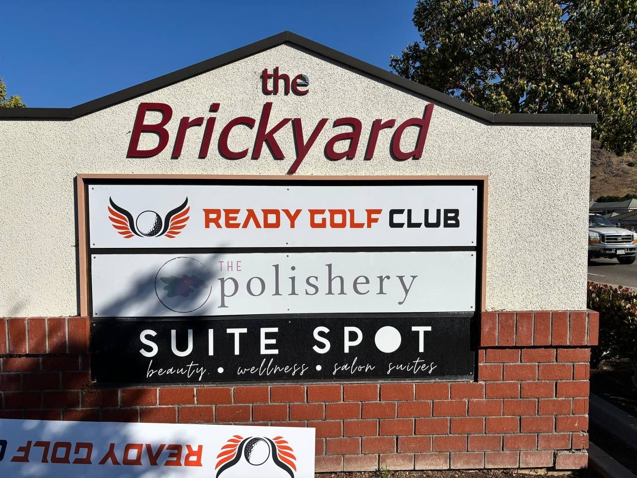 Brick sign for The Brickyard with business names: Ready Golf Club, The Polishery, and Suite Spot.