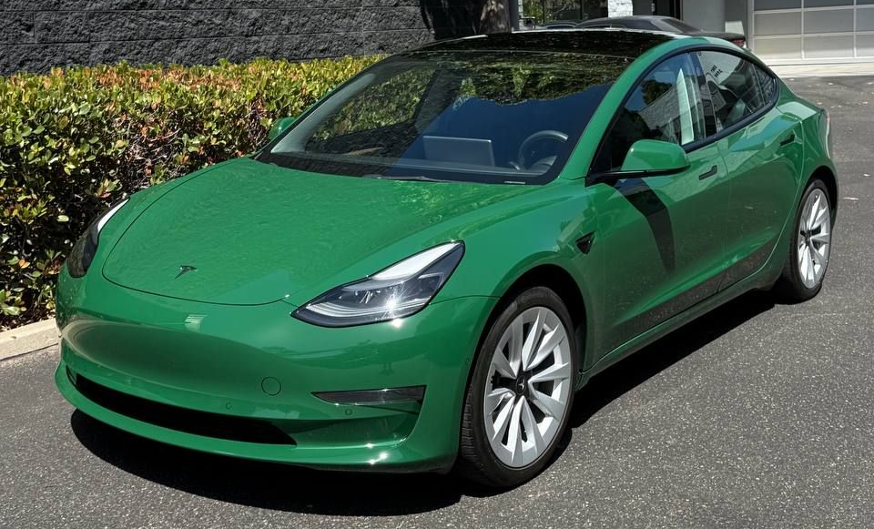 Green Tesla Model 3 parked outdoors on a sunny day