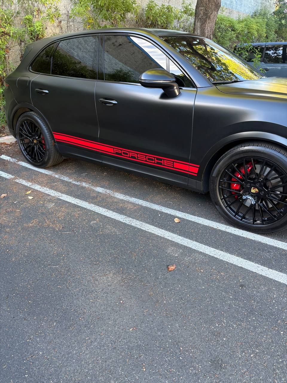 Black hatchback with red side stripe parked in a lot by trees