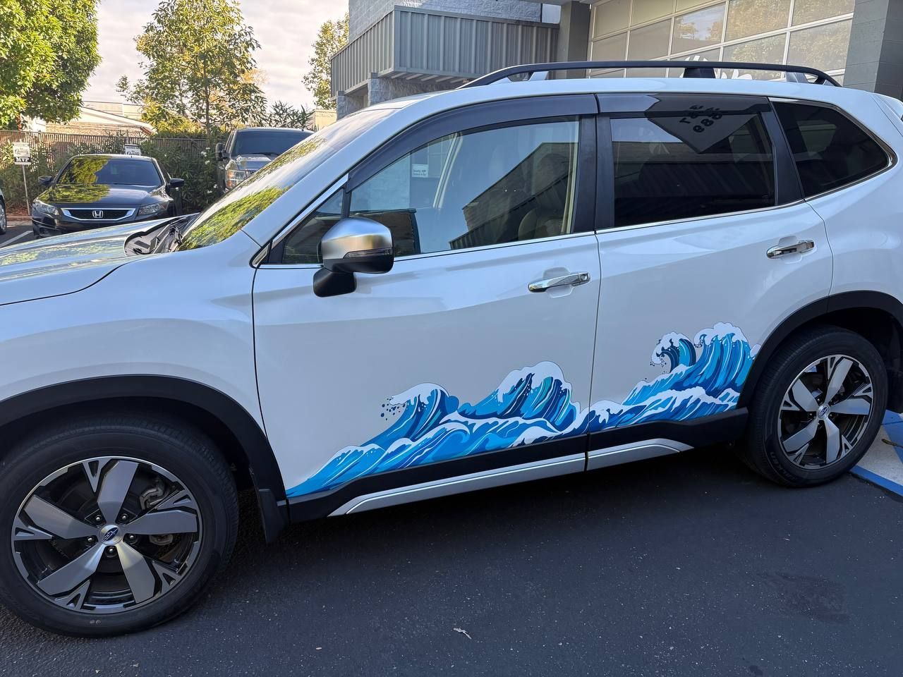 White SUV with blue wave graphics parked on a street near buildings and trees
