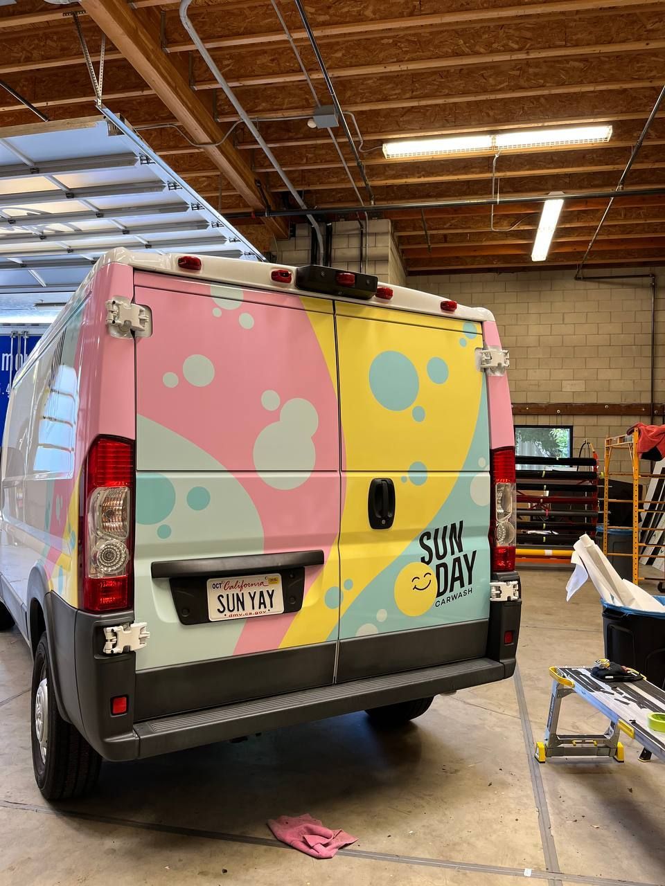 Colorful wrapped van in a warehouse, with pastel pink, yellow, and blue bubbles on the rear doors.