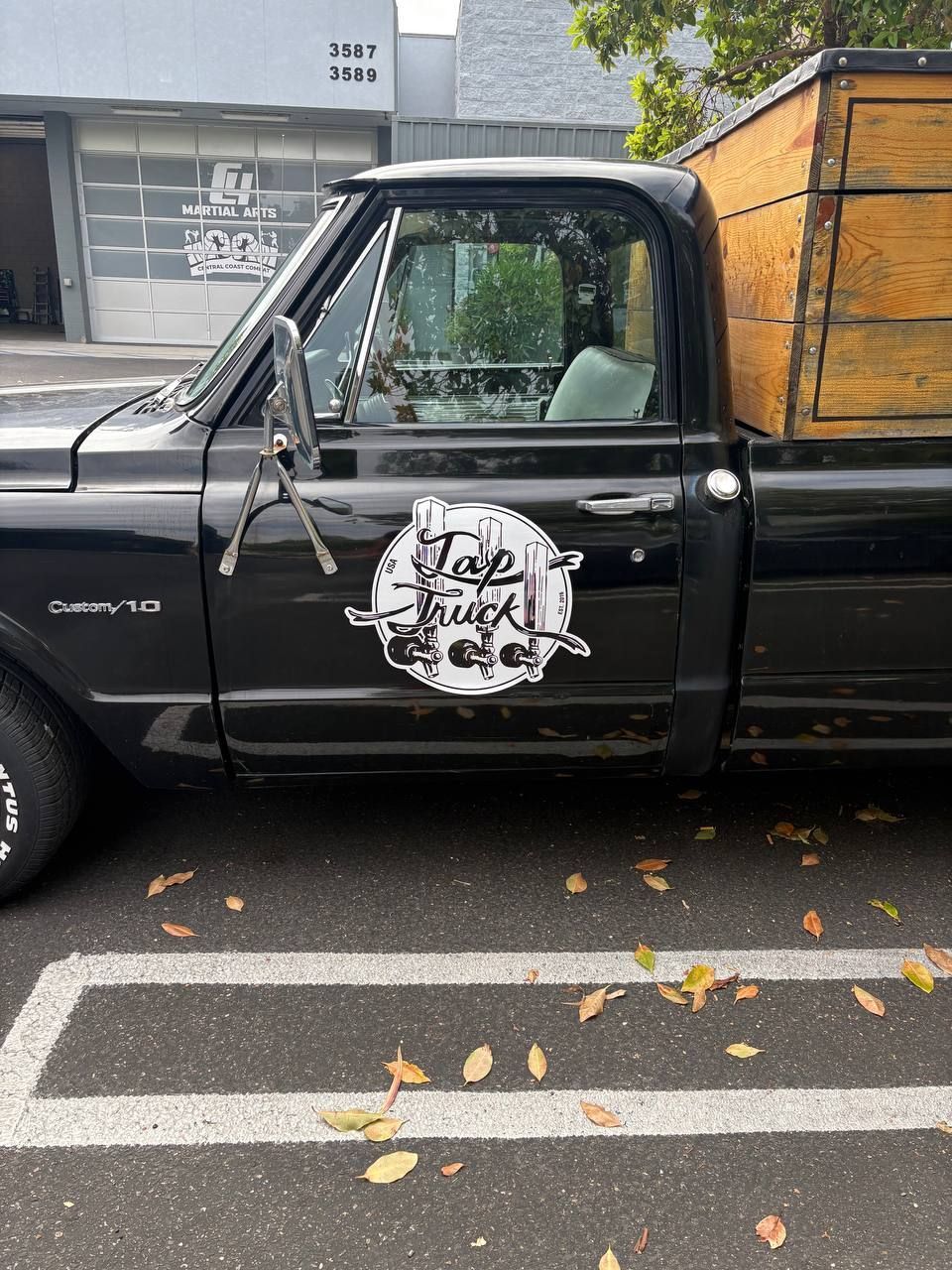 Black pickup truck parked on a wet street beside a building, with a white logo on the door.
