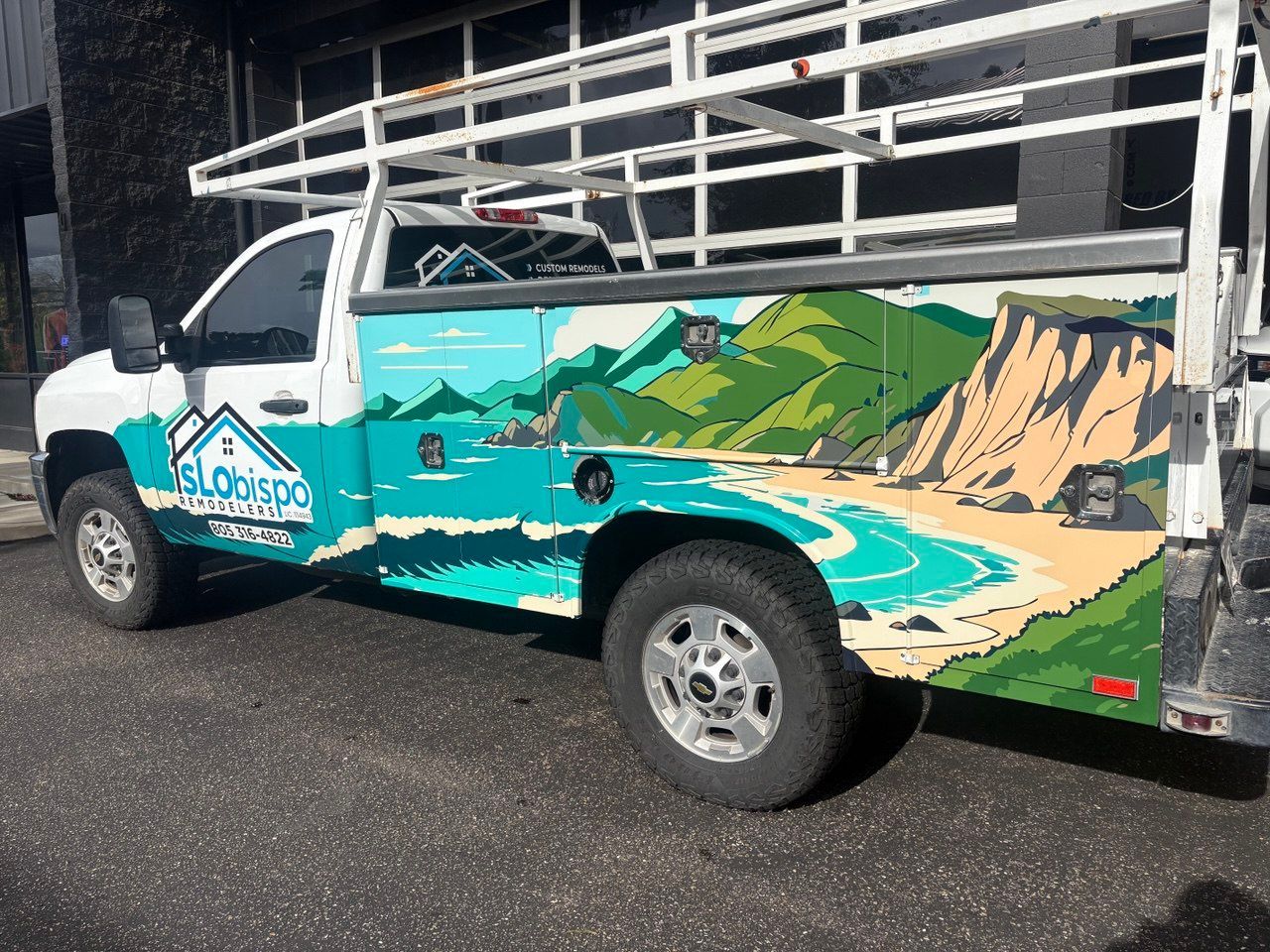 White pickup truck with colorful coastal mural and logo, parked beside a metal railing.