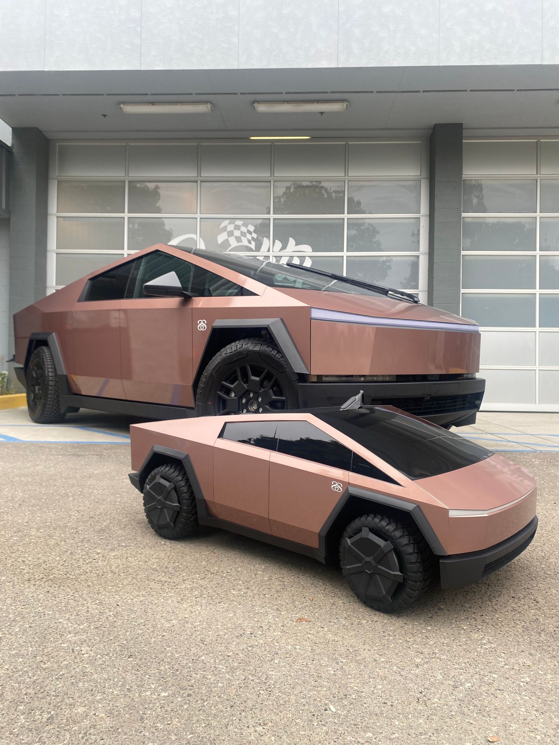 Two brown futuristic electric pickup trucks parked outside a building