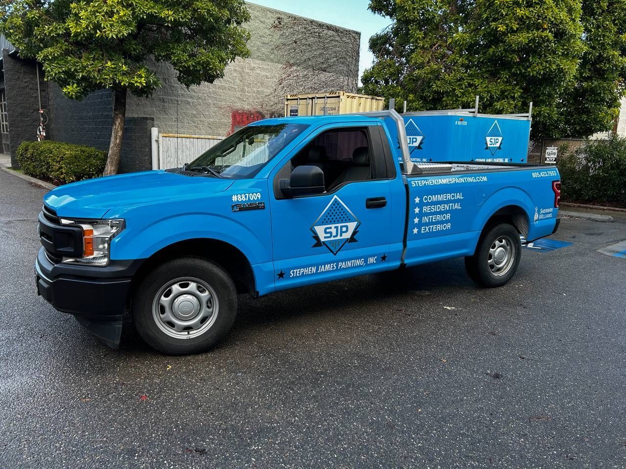 Blue pickup truck with utility bed parked outdoors on a wet lot