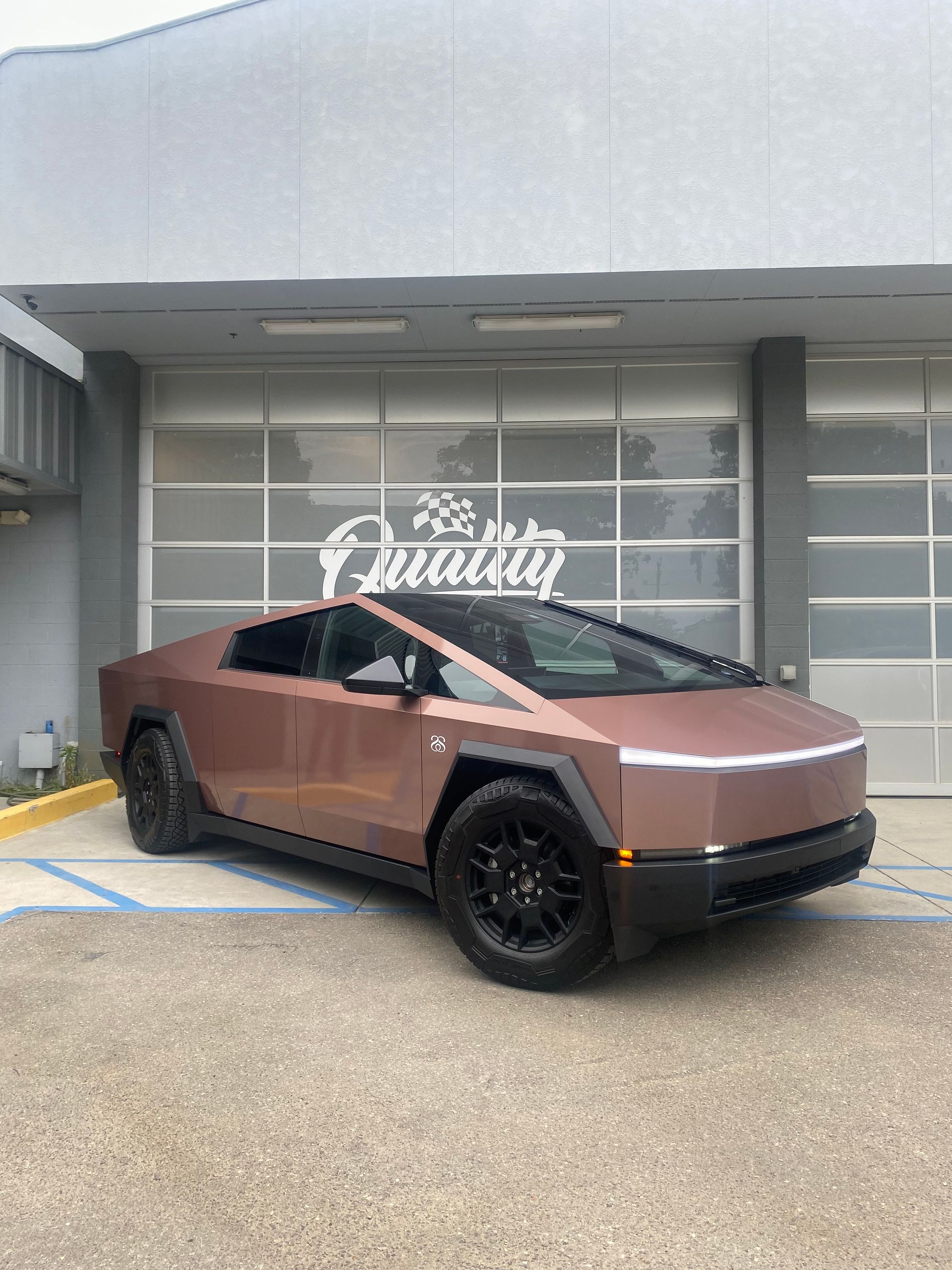 Bronze futuristic SUV parked outside a gray storefront with a white logo sign