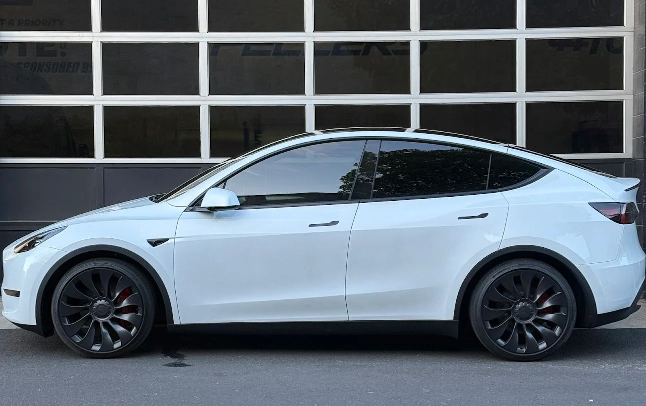 White Tesla Model Y parked in front of a garage door, side view