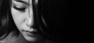 Close-up black-and-white portrait of a person looking downward, face partially obscured by hair