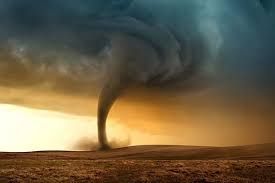 Dark tornado funnel over a barren field under stormy, golden clouds