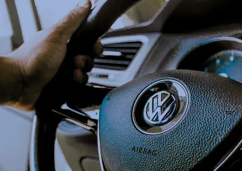 Hand on Volkswagen steering wheel inside car, with dashboard vents visible